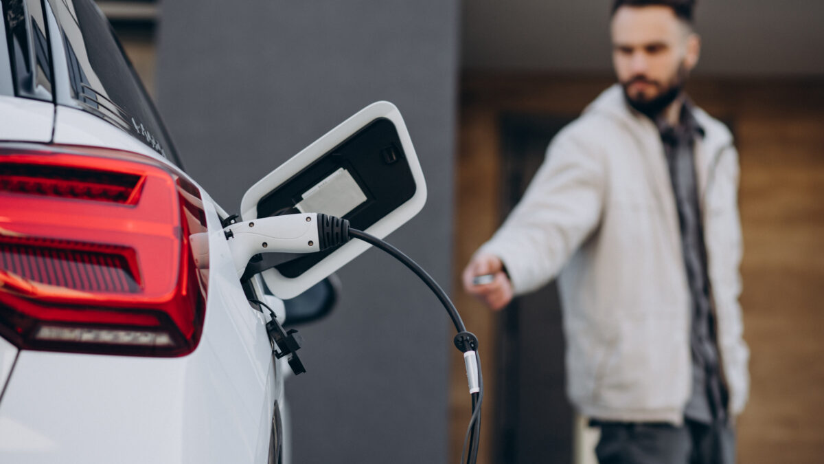 Un homme rechargeant une voiture électrique près de la maison