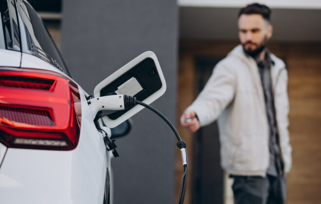 Un homme rechargeant une voiture électrique près de la maison