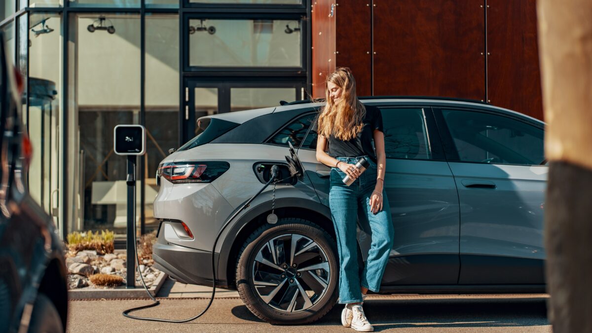 Une femme rechargeant sa voiture électrique via une borne de recharge sur pied de fixation.